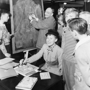 Margret & H.A. Rey signing books. Photo by anonymous (c. 1950). Wikimedia Commons.
