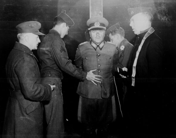 German General Anton Dostler is tied to a stake before his execution by firing squad. Guilty of ordering the execution of Allied soldiers in uniform under Hitler’s Commando Order. Photo by Blomgren (1 December 1945). U.S. National Archives and Records Administration. PD-US Government. Wikimedia Commons. 