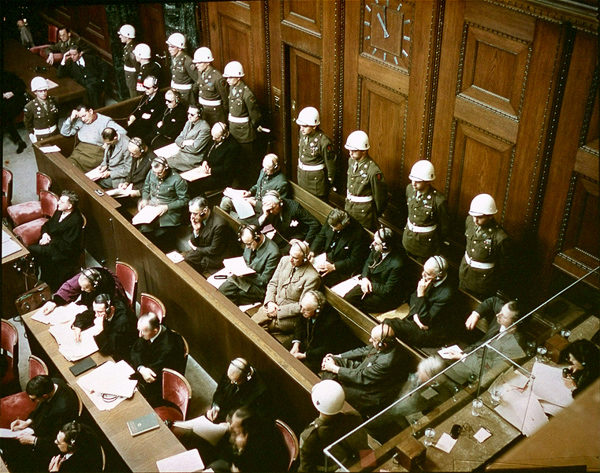 View of defendants in the dock at the International Military Tribunal trial (e.g., the main Nuremberg Trial). First row (left to right): Göring death/suicide), Hess (life), von Ribbentrop (death), Keitel (death), Rosenberg (death), Frank (death), Frick (death), Streicher (death), Funk (life), Schacht (acquitted); Back row (left to right): Döenitz (10 years), Raeder (life), von Schirach (20 years), Sauckel (death), Jodl (death), von Papen (acquitted), Seyss-Inquart (death), Speer (20 years), von Neurath (15 years), Fritzsche (acquitted); Missing: Kaltenbrunner (death); Bormann - tried in absentia (death); Krupp (case suspended); Ley (suicide prior to trial). Photo by Raymond D’Addario (November 1945). PD-US Government. Wikimedia Commons.