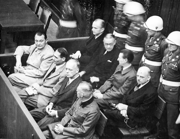 Nuremberg trial defendants in their dock. Front row (left to right): Göring (death/suicide), Hess (life), von Ribbentrop (death), Keitel (death); Back row (left to right): Döenitz (10 years), Raeder (life), von Schirach (20 years), Sauckel (death). Photo by US Army (c. 1945−46). National Archives and Records Administration. PD-US Government. Wikimedia Commons. 
