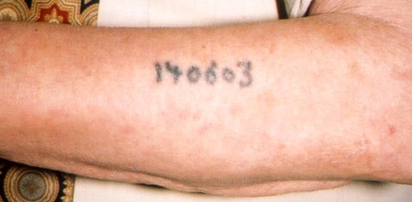 Auschwitz survivor Sam Rosenzweig displays his identification tattoo. Photo by Rudy Purificato (date unknown). PD-U.S. Government. Wikimedia Commons. 