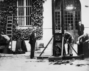 Workmen in La Sante Prison courtyard cleaning and dismantling the guillotine, 25 May 1946, after the execution of Marcel Petiot. Blood is visible on the pavement in the foreground at the base of the guillotine. Photo by anonymous (25 May 1946).
