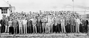 Project Paperclip Team (Von Braun Rocket Team) at Fort Bliss. Front Row: Arthur Rudolph (4th from left), Wernher von Braun (7th from left); Fourth Row: Kurt Debus (first on left, looking away from camera); Missing: Dorenberger and Rickhey. Photo by anonymous (c. 1946). PD-U.S. Government. Wikimedia Commons. 
