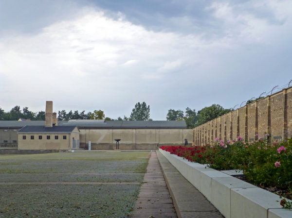 Ravensbrück concentration camp. Crematorium (with smokestacks) can be seen in the background. Buildings housing the inmates have been demolished. Photo by Wald1siedel (2015). PD-CCA-Share Alike 4.0 International. Wikimedia Commons.