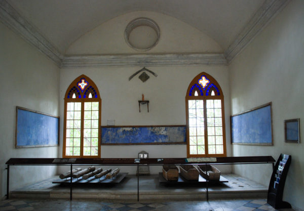 Interior of Fort Mont-Valérien chapel. Boxes on the right were used to transport the bodies of the executed victims to their graves. On the left are the poles used to tie up the victims in the clearing before being shot. The bluish murals are an attempt to preserve the prisoners’ graffiti which is being slowly damaged by humidity. Photo by Sandy Ross (2017).