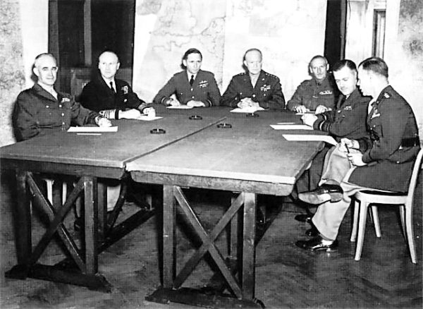 Allied invasion planners. From left to right: General Bradley, Admiral Ramsay, Air Chief Marshal Tedder, General Eisenhower, General Montgomery, Air Chief Marshal Leigh-Mallory, and General Smith. Photo by anonymous (c. 1944). PD-Expired Copyright. Wikimedia Commons.
