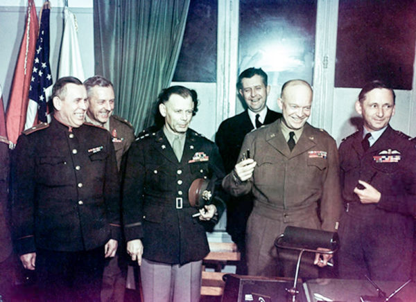 Senior Allied commanders immediately after the Germans surrendered at Reims, France. General Eisenhower (holding pens) is flanked by General Walter Bedell Smith (left) and Air Chief Marshal Arthur Tedder (right). Behind Eisenhower is Captain Harry Butcher. Photo by Army Signal Corps. (7 May 1945). PD-US Government. Wikimedia Commons.