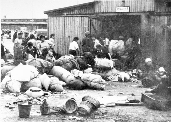 The “Kanada” barracks in Auschwitz. The warehouses contained the looted belongings of prisoners, including those sent to the gas chamber on arrival. Photo by SS officers Walter and Hofmann (c. May/June 1944). U.S. Holocaust Memorial Museum. PD-Expired Copyright. Wikimedia Commons.