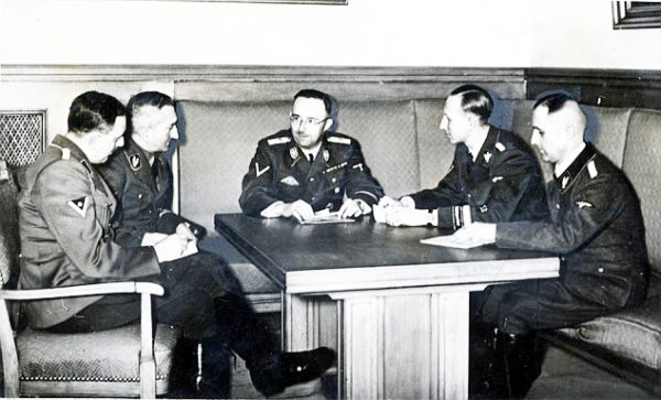 Heinrich Himmler meeting with the heads of the Gestapo. Left to right: Franz Josef Huber, Arthur Nebe, Himmler, Reinhard Heydrich, and Heinrich Müeller. The meeting was to plan the investigation of an attempted assassination of Hitler a day earlier. Photo by anonymous (9 November 1939). Bundesarchiv Bild 183-R98680/CC-BY-SA 3.0. PD-CCA-Share Alike 3.0 Germany.
