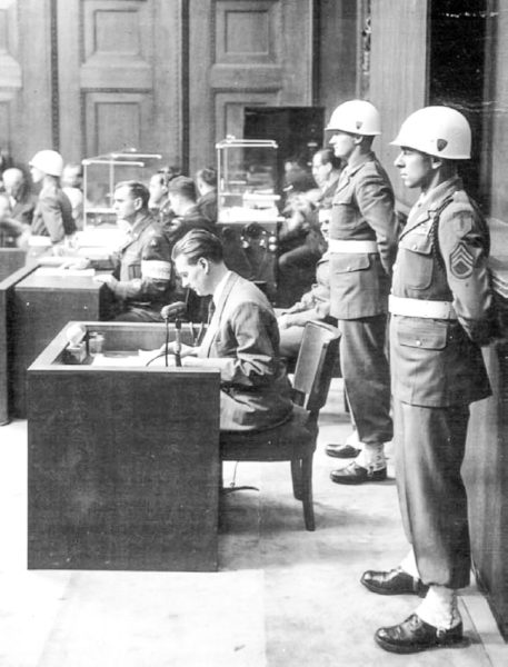 Staff Sgt. Emilio (Leo) DiPalma stands guard with his arms folded behind him next to the witness box (foreground) at the Nuremberg Trial. Photo by anonymous (c. 1945/46). Emily Aho. PD-U.S. Government. 