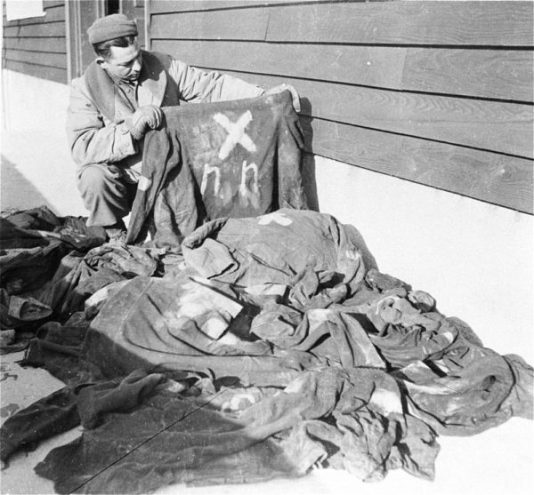 Soldier looking at prisoner clothing at Natzweiler-Struthof concentration camp. These are uniforms worn by Nacht und Nebel inmates as identified by the NN. Photo by anonymous (December 1944). PD-U.S. Government. Wikimedia Commons. 