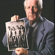 Wilhelm Brasse holding one of the photographs he took in Auschwitz. Photo by anonymous (c. 2005). ©️Rekontrplan Film Group. Portrecista. PD-Fair use. Wikimedia Commons.