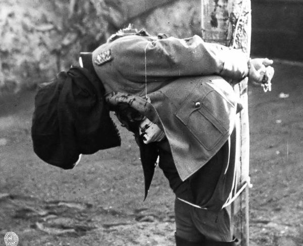 Anton Dostler’s body slumps toward the ground after being executed by a firing squad in the Aversa (Italy) stockade. His hands still grip a rosary. Photo by anonymous (1 December 1945). PD- U.S. Government. Wikimedia Commons.