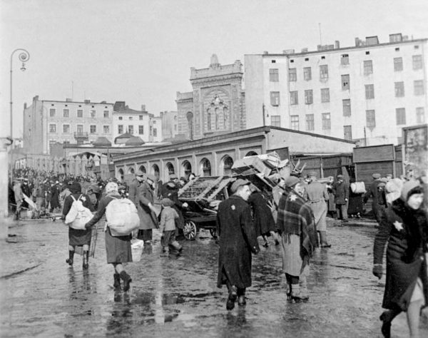 Jews being deported from the Łódź Ghetto (city was named Litzmannstadt during the German occupation). The synagogue in the middle of the image no later exists as it was destroyed by the Germans in November 1940. Photo by anonymous (c. March 1940). German Federal Archives. PD-Bundesarchiv, Bild 137-051639A/CC-BY-SA 3.0. Wikimedia Commons.