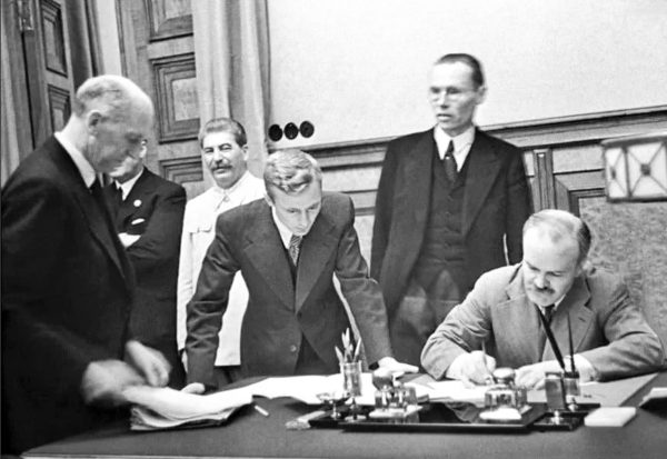 After invading Poland on 17 September, Soviet foreign minister, Molotov, signs an agreement on friendship with Germany. Stalin stands in the background (white coat). Photo by Mikhail Kalashnikov (28 September 1939). PD-Russian release. Wikimedia Commons.