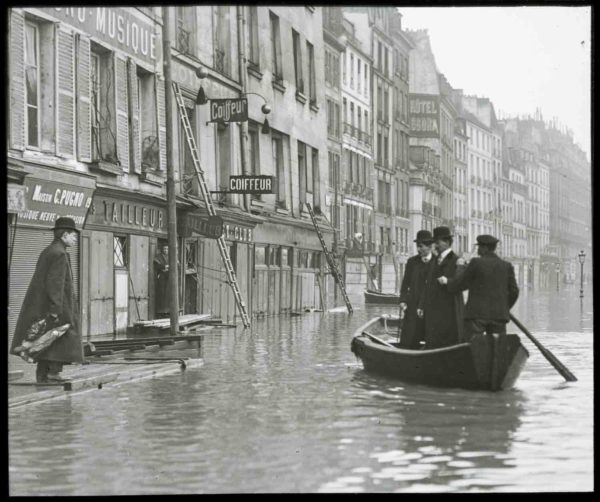 Flooded street during the Great Flood of Paris of 1910. Photo by anonymous (c. 1910). Licensed under the Licence Ouverte. Wikimedia Commons.