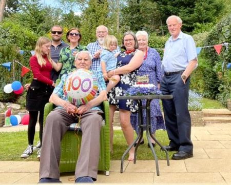 Family photo at Stan’s 100th birthday celebration. Left to right: Sennen Vinycomb (great-granddaughter), Chris Vinycomb (grandson), Jo Vinycomb (Chris’s spouse), Graham Booker (nephew), Isla Vinycomb-Brown (great-granddaughter), Claire Vinycomb-Brown (granddaughter), Pat Vinycomb (daughter), and Keith Vinycomb (son-in-law). Stanley Booker seated in front. Photo by Kieran Vinycomb-Brown (Claire’s spouse; 24 April 2022). Courtesy of Pat Vinycomb. 