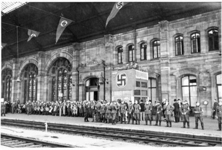 Interior view of station taken from across the tracks during the Occupation. Alsatian refuges wait on the main platform while guarded by German troops. Photo by anonymous (c. 1940). ©️ Archives de Strasbourg.