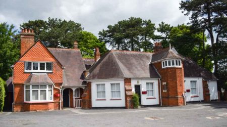 Exterior view of the stable yard cottages where Dilly Knox and Alan Turing lived at Bletchley Park. The brick tower separates Knox’s apartment on the left with Turing’s apartment on the right. The room at the top of the tower is where Turing broke the Enigma code. Photo by Sandy Ross (13 June 2022).