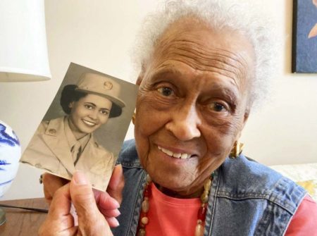 Romay Davis, 102, poses with a photo showing her in World War II. Photo by Jay Reeves (c. July 2022). AP Photo.
