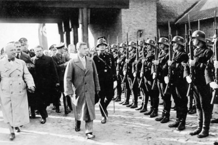 The Duke of Windsor inspecting the SS training facility at Ordensburg Krössinsee. Robert Ley in white trench coat is on the far left. Photo by Georg Pahl (13 October 1937). Bundesarchiv, Bild 102-17964/Pahl, Georg/CC-BY-SA 3.0. PD-CCA-Share Alike 3.0 Germany. Wikimedia Commons.