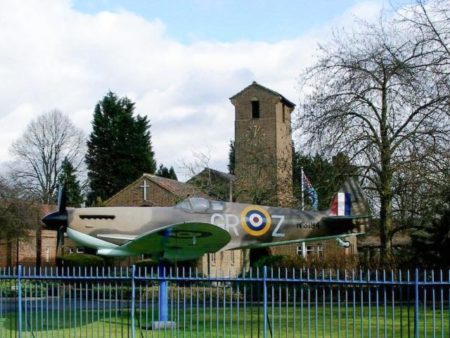 Entrance to church at Biggin Hill airport. This is a mock-up of a Spitfire fighter aircraft. Photo by tristan forward (c. August 2006). PD-CCA-Share Alike 2.0 Generic. Wikimedia Commons.