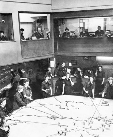 The operations room at RAF Fighter Command’s No. 10 Group headquarters, Rudloe Manor, Wiltshire. WAAF plotters and duty officers are seen at work. Photo by flight Officer A. Goodchild (c. 1943). Air Ministry Second World War Official Collection. PD-U.K. public domain. Wikimedia Commons.