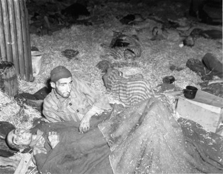 Two survivors of Nordhausen lie among corpses on the straw-covered floor the barracks.