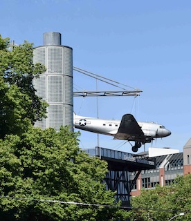 American DC-7 airplane commemorating the Berlin Airlift. The plane is suspended from struts above a commercial plaza in Berlin. Photo by Sandy Ross (c. November 2023).
