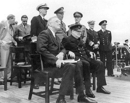 President Roosevelt (seated left) and British Prime Minister Winston Churchill (seated right) on the deck of the HMS Prince of Wales. Standing behind the two leaders are George C. Marshall (seconded from left) and Adm. Harold Stark (second from right). Photo by anonymous (10 August 1941). U.S. Naval Historical Center. PD-U.S. Government. Wikimedia Commons.