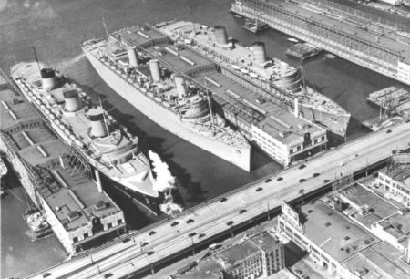 The three largest ocean liners docked together in New York. The SS Normandie (left) is docked at Pier 88 in mid-town. The RMS Queen Mary (center) and RMS Queen Elizabeth are docked at Pier 90. The QE arrived on 7 March 1940 and two weeks later, on 21 March, the QM left. Photo by anonymous (c. March 1940). Ships Nostalgia. https://www.shipsnostolgia.com/media/normandie-queen-mary-and-queen-elizabeth-troopships-ww2.258317/