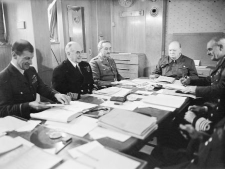 Winston Churchill and his chiefs of staff around a conference table aboard the RMS Queen Mary enroute to the United States. Left to right: Air Marshal Sir Charles Portal, Admiral of the Fleet Sir Dudley Pound, Gen. Sir Alan Brooke, and Prime Minister Winston Churchill. Photo by Harold Tomlin (c. May 1943). Imperial War Museum. PD-Expired copyright. Wikimedia Commons.