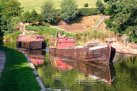 Historical working narrowboats on the Macclesfield Canal in Cheshire, England. The motorized boat is towing the butty. Photo by G-Man (c. 2005). PD-Author release. Wikimedia Commons.