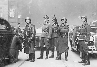 SS-Gruppenführer Jürgen Stroop (fourth from right) and his entourage viewing the destruction on Nowolipie Street in the Warsaw Ghetto. Image was discovered in the Stroop Report. Photo likely by Franz Konrad (c. 19 April – 16 May 1943). National Archives and Records Administration. PD-Poland Public Domain. Wikimedia Commons.