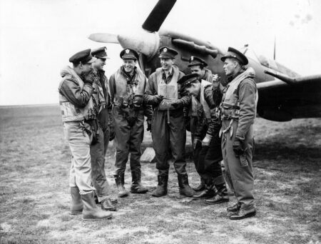 Pilots from the 4th Fighter Group in front of a Spitfire at RAF Debden airbase. The pilot in the center holding a pipe is Lt. Col. Chesley G. Peterson. The Spitfire is Peterson’s aircraft. Photo by anonymous (c. 1943). American Air Museum. PD-U.S. Government. Wikimedia Commons.