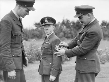 Three American pilots of No. 71 Eagle Squadron RAF: Left to right: Pilot Officers G. Tobin, V.C. “Shorty” Keough, and A. Mamedoff. They are showing off their new squadron badge at RAF Church Fenton. Photo by anonymous (c. 1940). Imperial War Museum. PD-U.K. Government public domain. Wikimedia Commons.